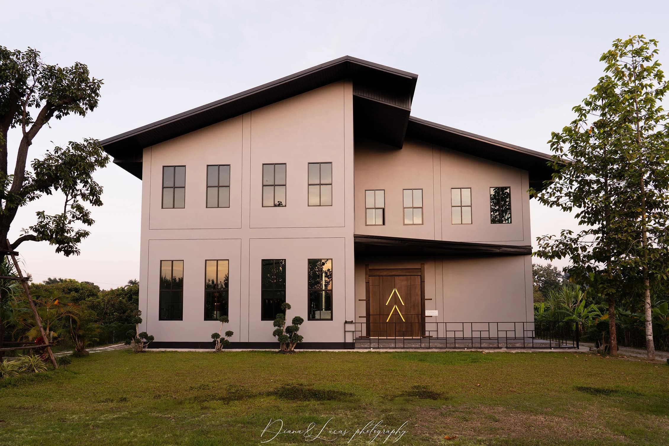 โรงกลั่นทันสมัยสองชั้น ผนังสีขาว หน้าต่างบานใหญ่ หลังคาทรงลาดสีเข้ม ตั้งอยู่บนสนามหญ้ามีต้นไม้ยามพระอาทิตย์ตก