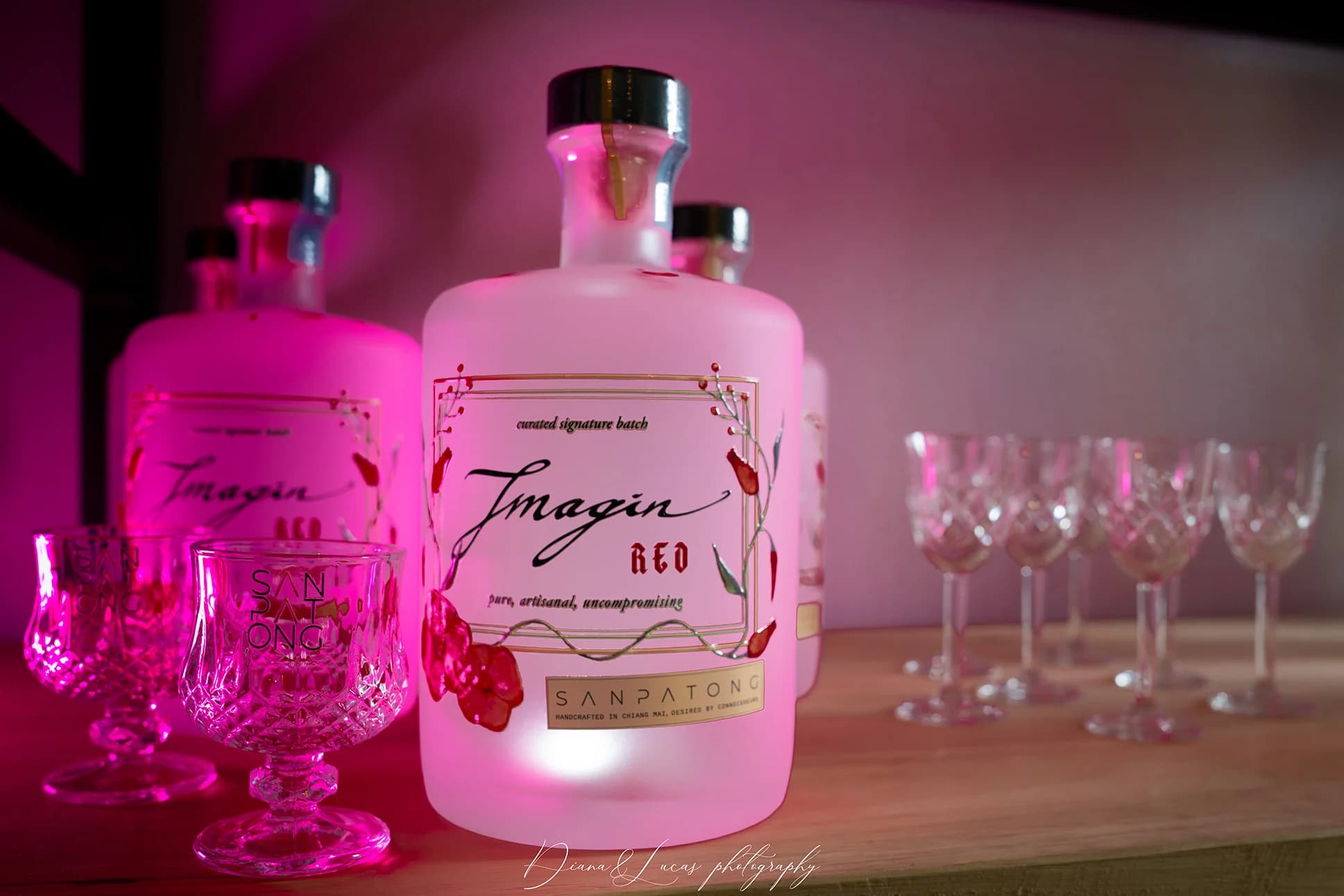 Frosted liquor bottles on a bar shelf with pink lighting, featuring a label reading “Imagine Red,” with crystal glasses in the background.